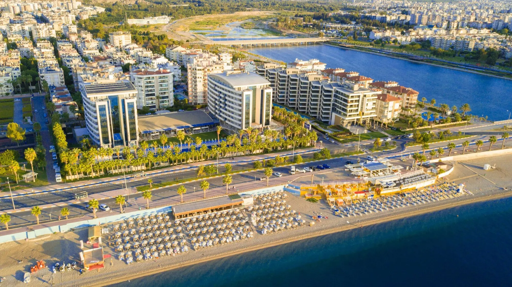 Въздушна гледка към хотела, крайбрежната улица и плажа с чадъри – Porto Bello Hotel Resort & Spa, Лара Кунду