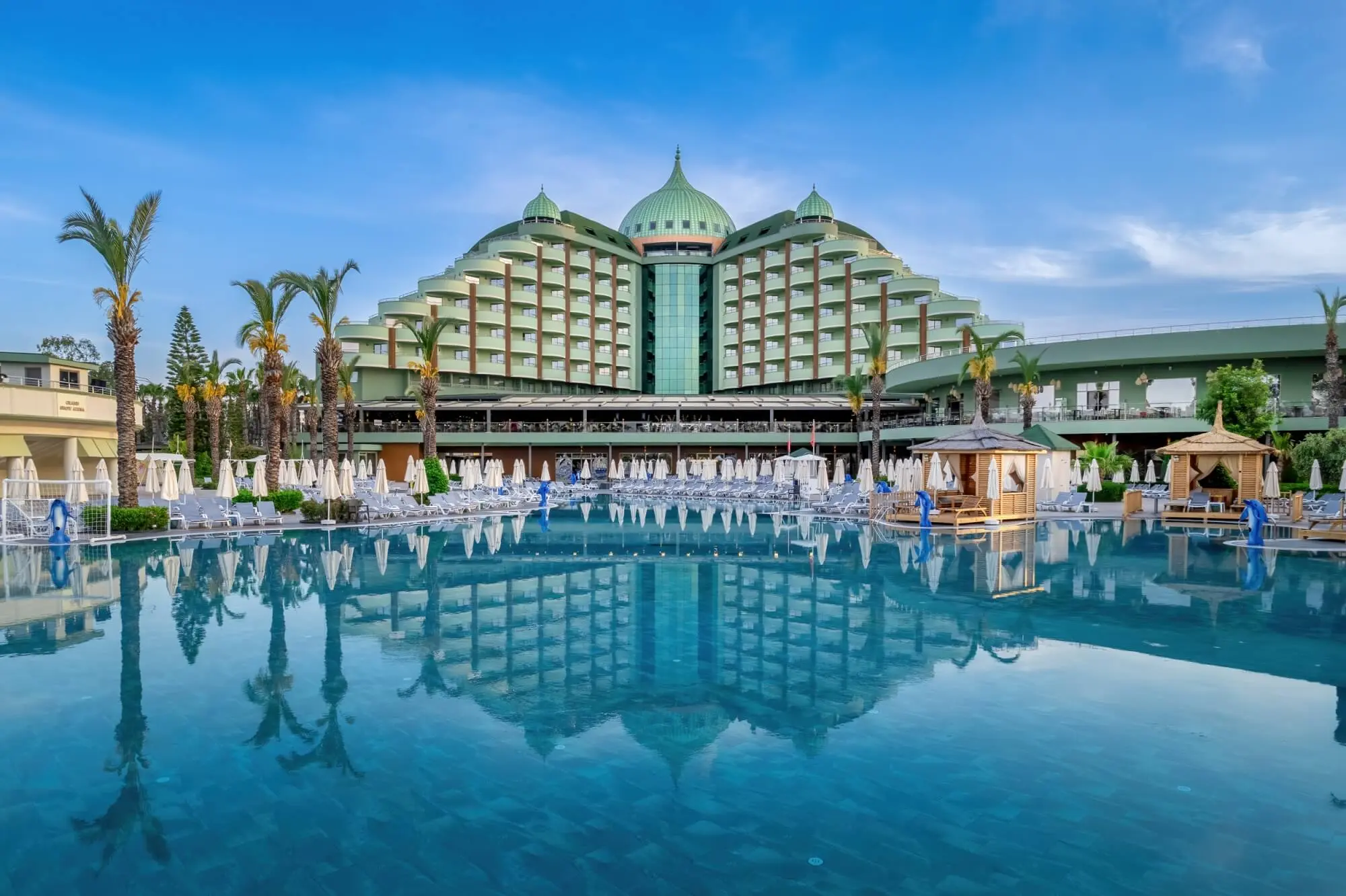 Основната сграда с куполи, отразена в големия открит басейн сред палми – Delphin Palace, Лара Кунду