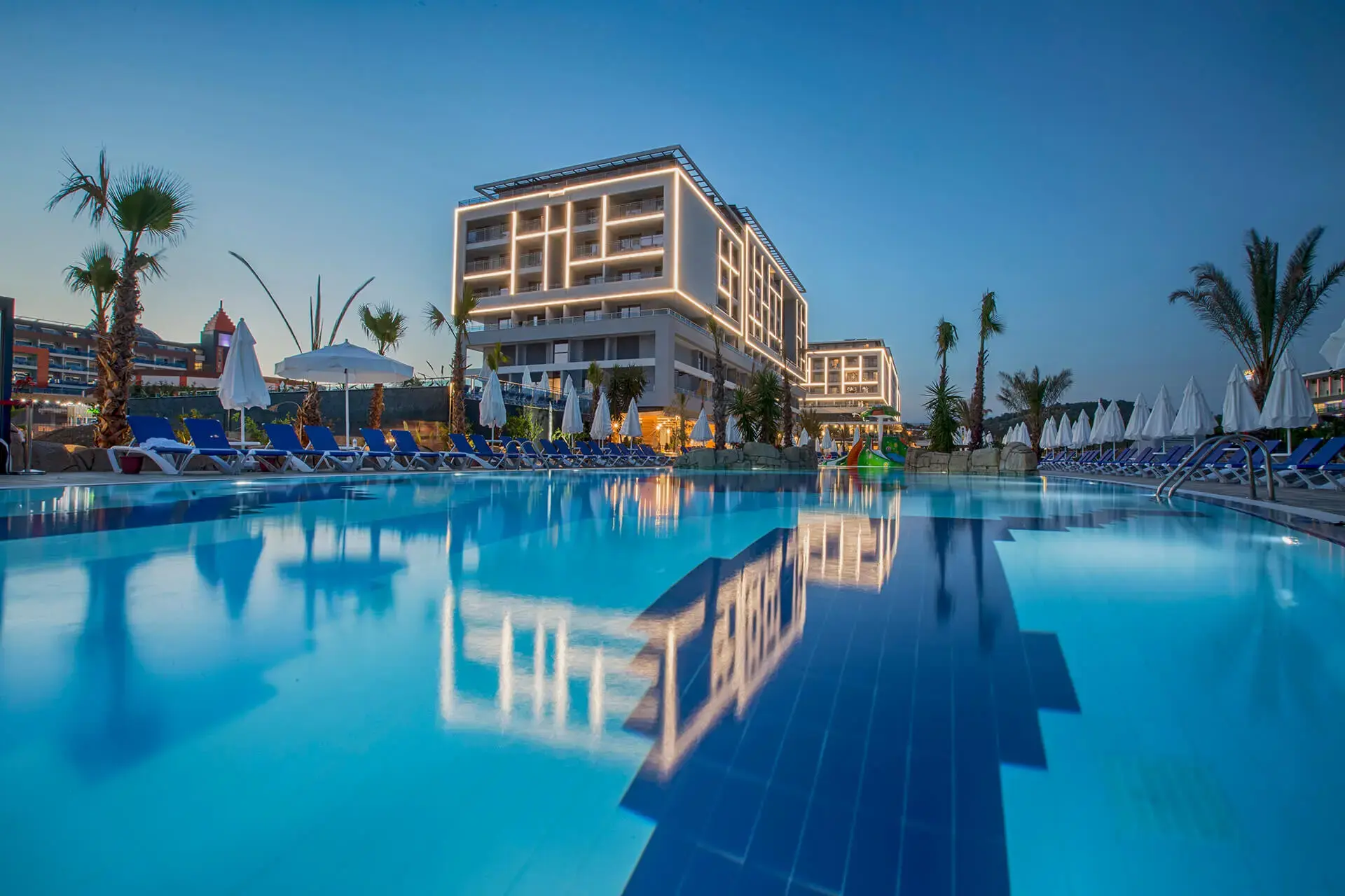 Басейн с отражение на хотелската сграда по здрач и палми край него – Numa Bay Exclusive, Алания