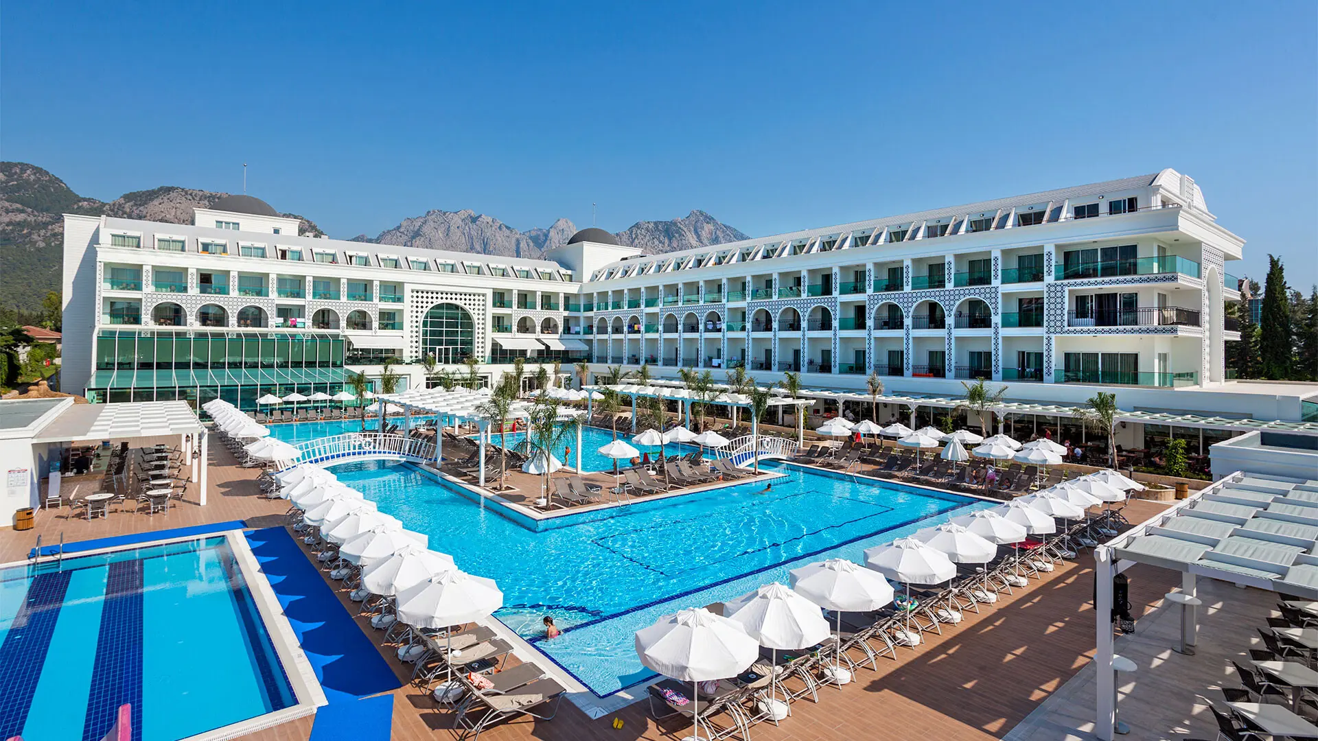 Фасадата на хотела и басейнът с чадъри пред нея – Karmir Resort and SPA, Кемер