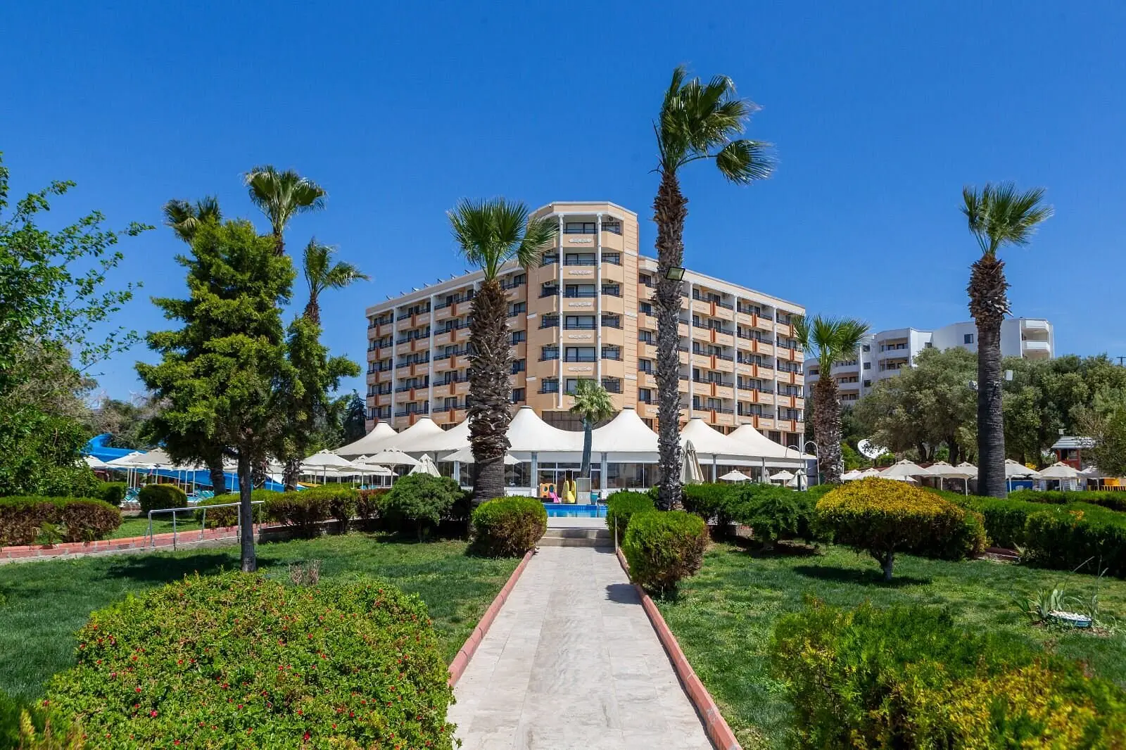 Алея през градината с палми и цветни храсти към хотелската сграда – The Holiday Resort Hotel, Дидим