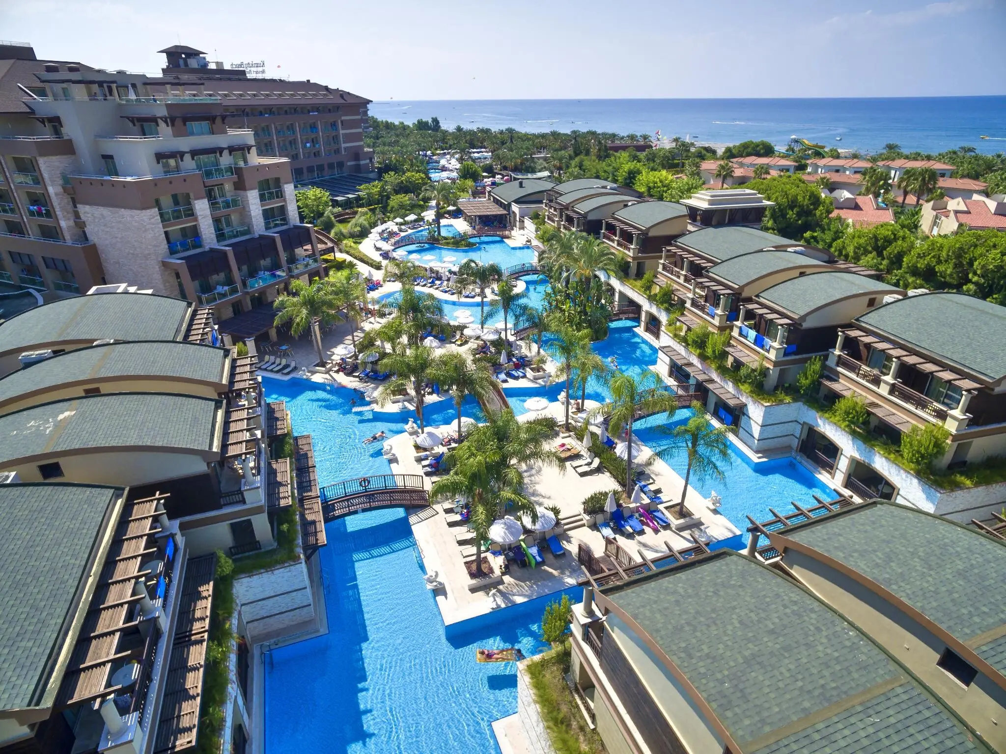 Басейн с палми сред сградите на хотела и морето в далечината – Sunis Kumkoy Beach Resort & Spa, Сиде