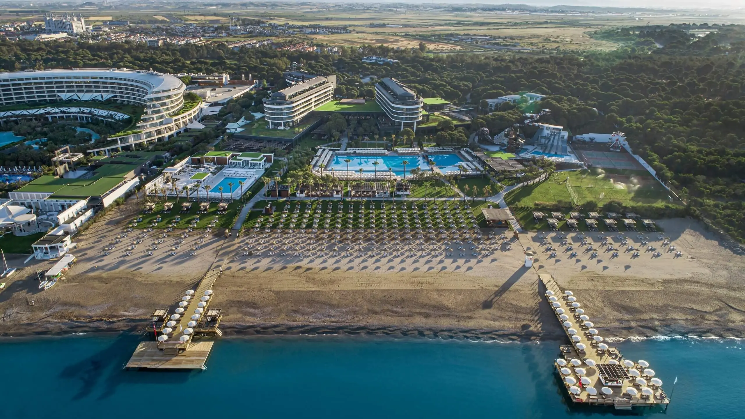 Въздушен изглед към хотела, плажа и двата кея на морския бряг – Voyage Belek Golf & Spa, Белек