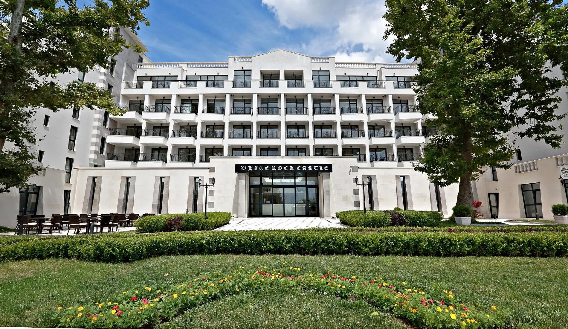 Бялата фасада с цветни лехи и зелена морава пред входа – White Rock Castle Suite Hotel & Spa, Балчик