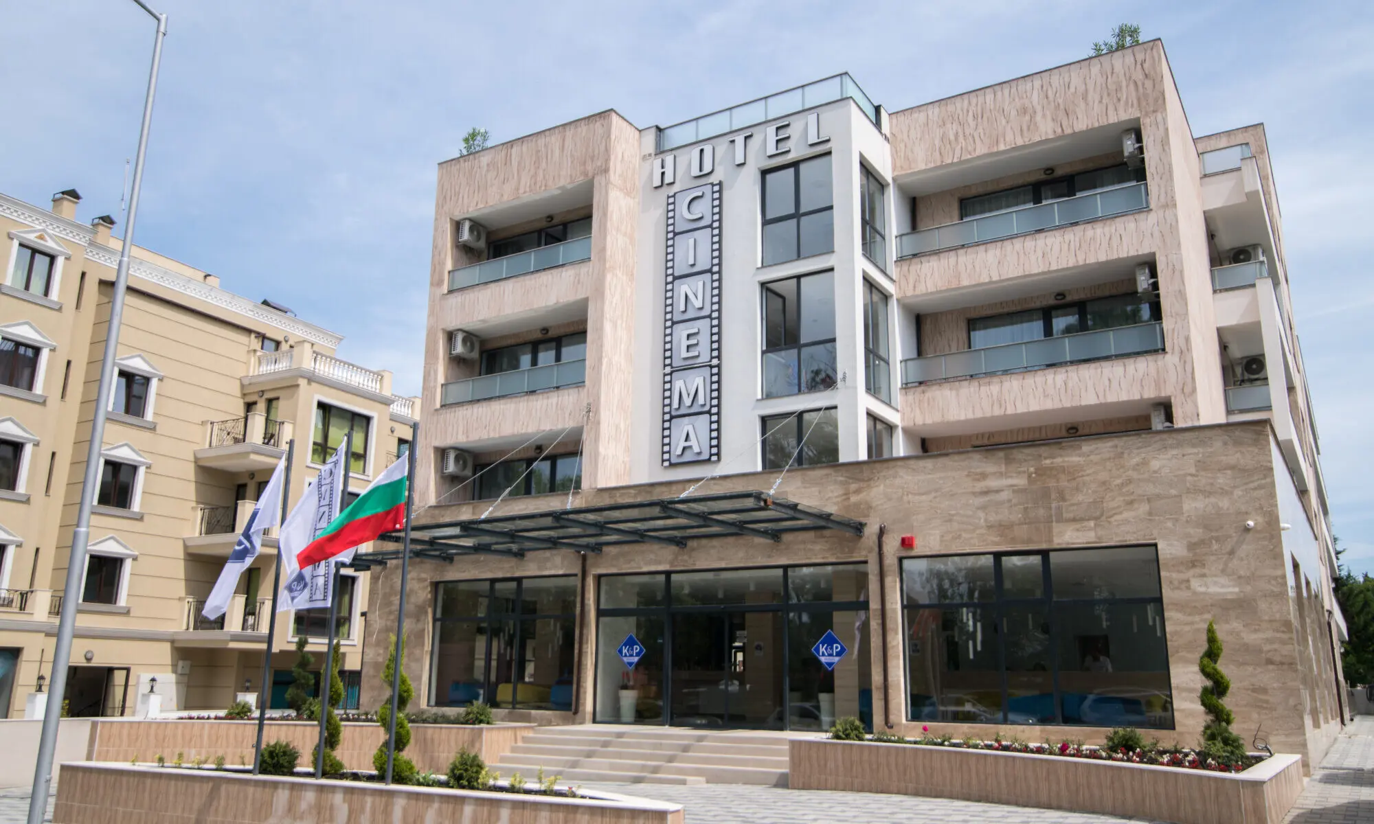 Входът и модерната фасада на хотела със знамена пред сградата – Хотел Синема, Приморско