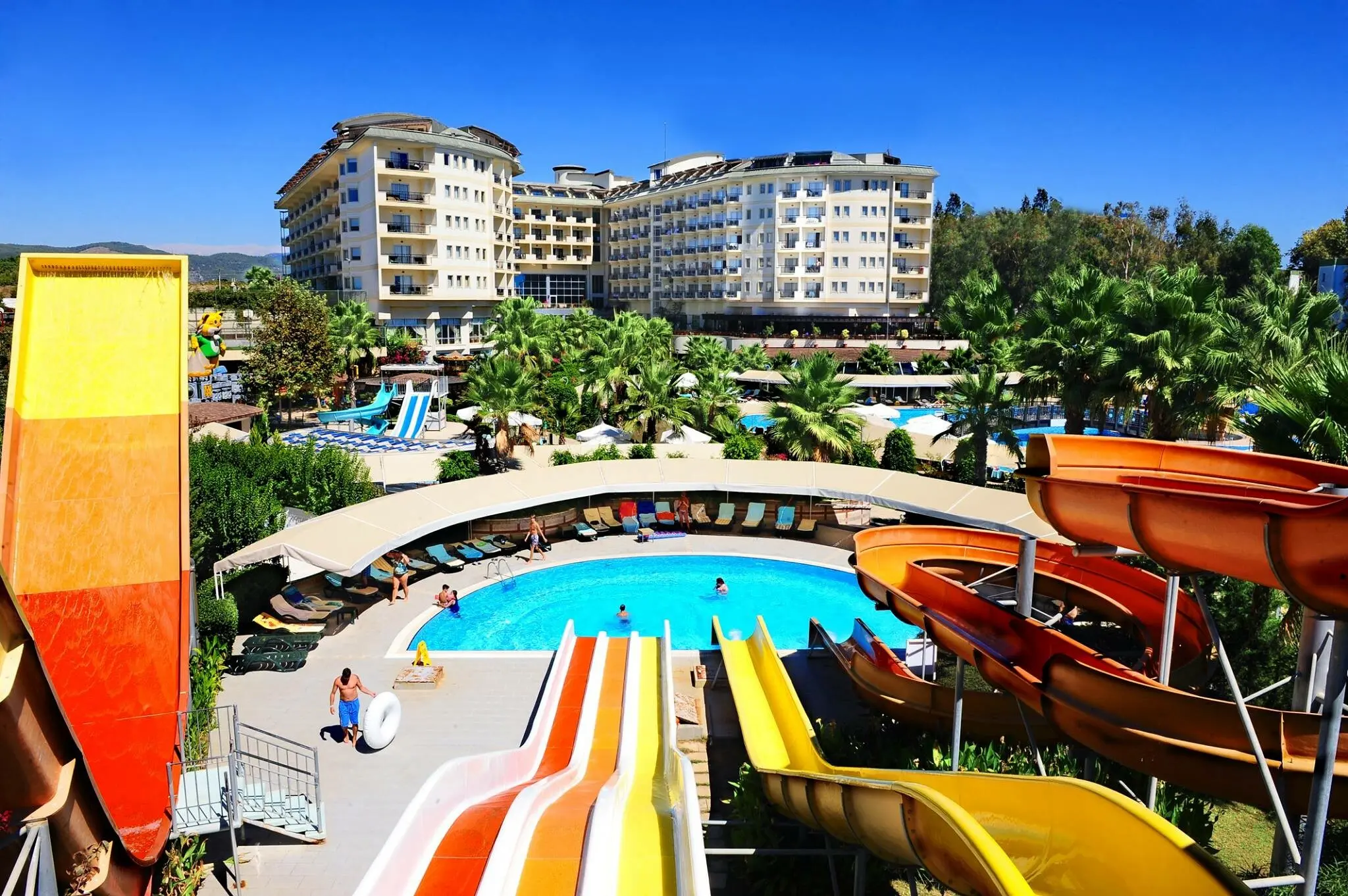 Басейн с цветни водни пързалки пред хотелския корпус – Mukarnas Spa Resort, Алания