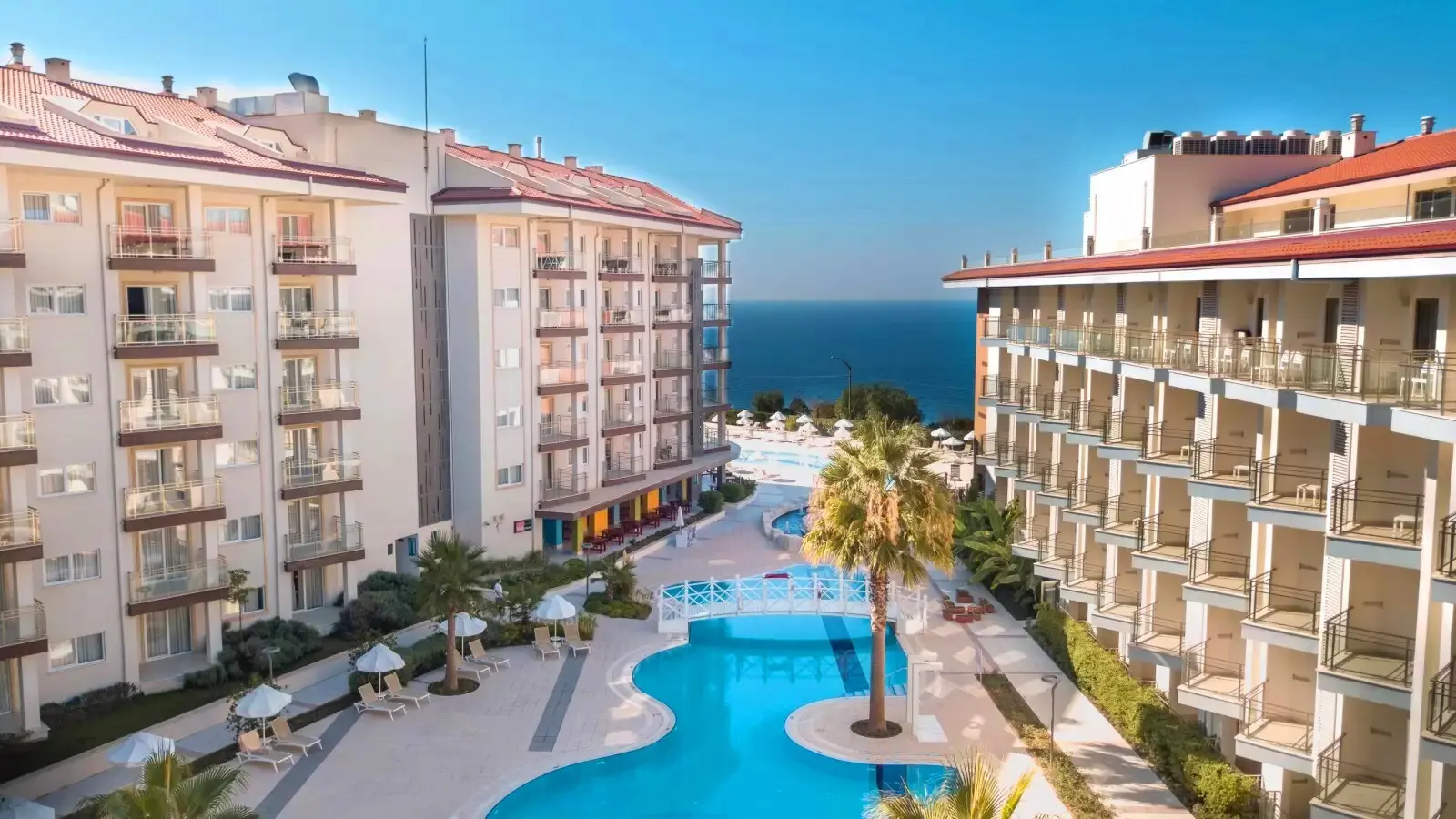 Басейн с палми между хотелските блокове и изглед към морето – Ramada Hotel & Suites by Wyndham, Кушадасъ