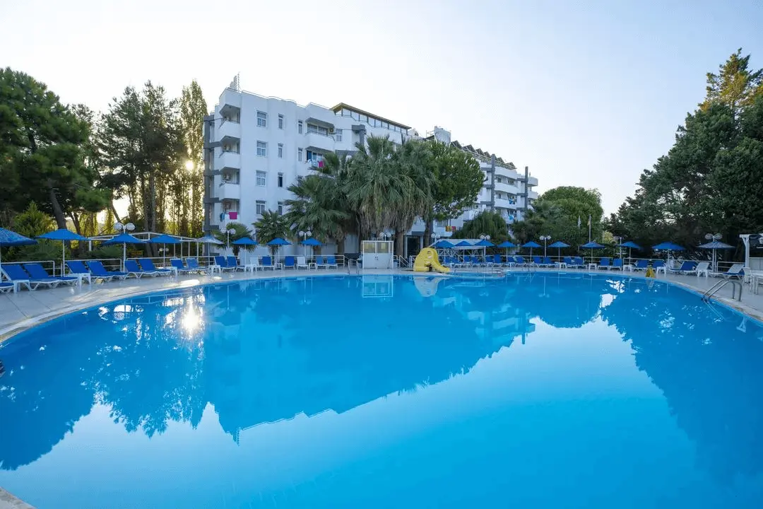 Голям открит басейн с шезлонги пред хотелския корпус сред борове – Flora Suites, Кушадасъ