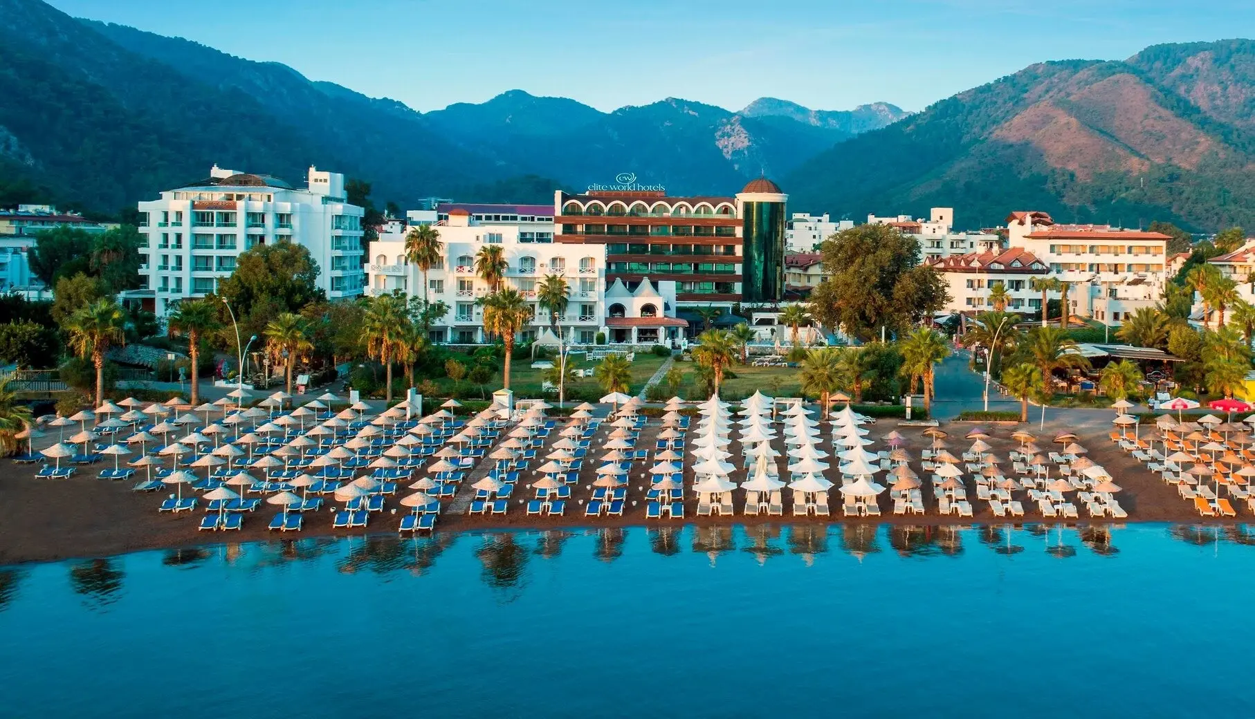 Плаж с чадъри и шезлонги, а зад него хотелът и планини над залива – Elite World Marmaris (16+), Мармарис