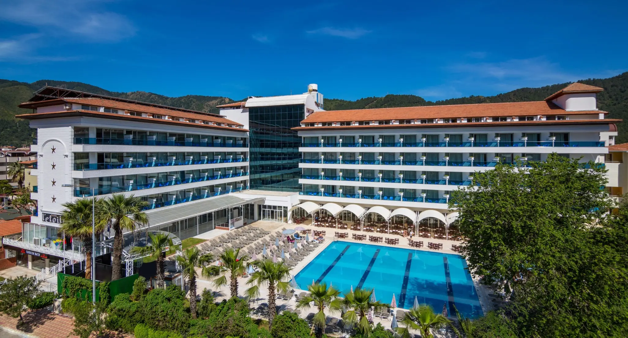 Сградата на хотела с открит басейн, палми и планини зад нея – L' etoile Beach Hotel, Мармарис