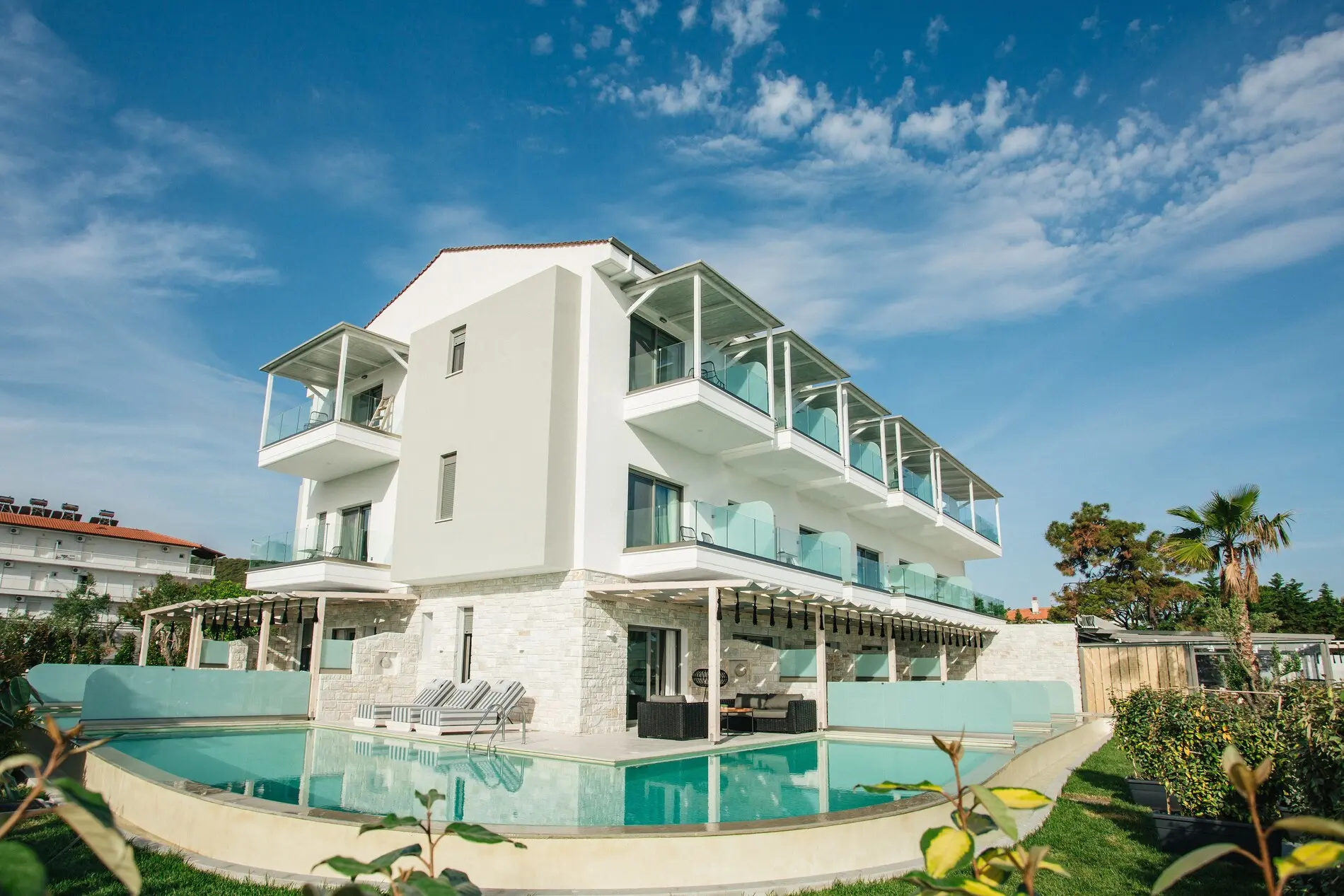 Бяла сграда със стъклени балкони и басейн отпред – Blue Carpet Luxury Suites, Касандра