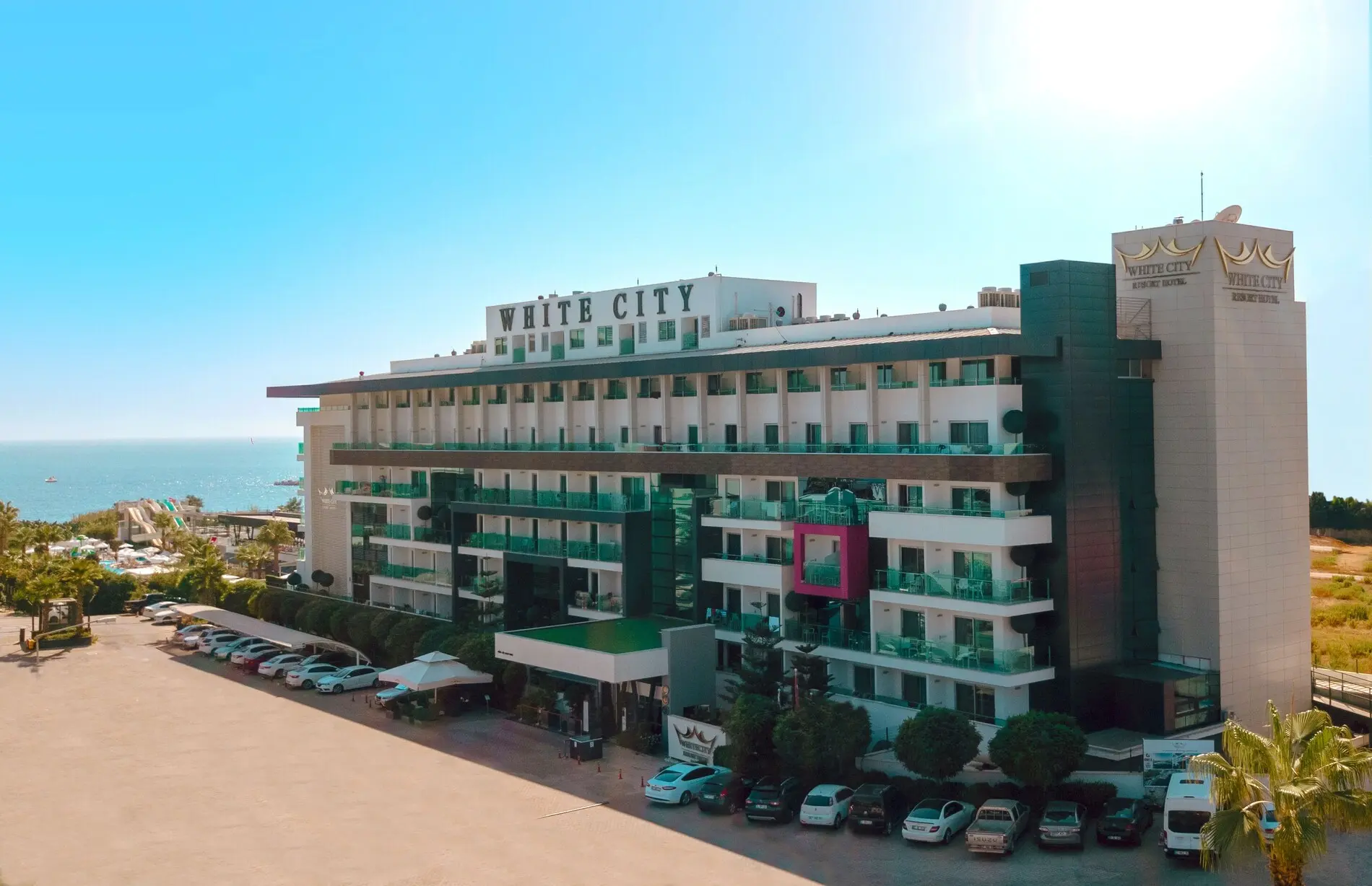 Външен изглед към хотела с паркинг и морето отдалеч – White City Resort Hotel, Алания