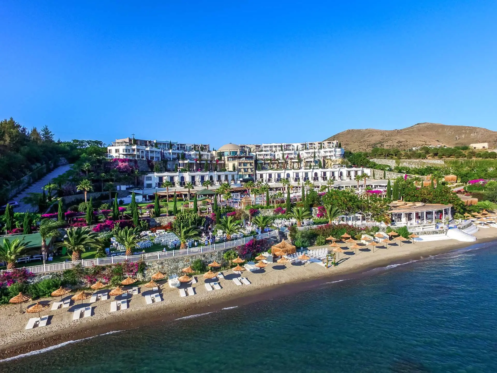 Плажна ивица с шезлонги пред хотела и зелените хълмове над залива – Sianji Wellbeing Resort, Бодрум