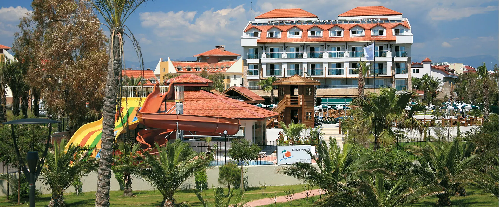 Хотелска сграда с червени керемиди, палми и озеленени дворове – Seher Resort & SPA, Сиде