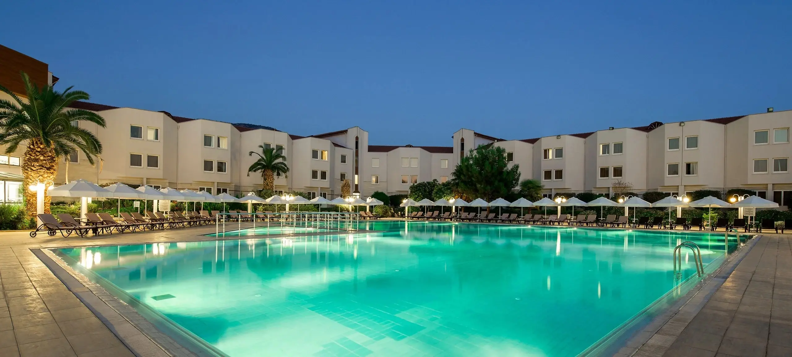 Открит басейн по здрач с осветени бели сгради и палми – Richmond Thermal & Spa Hotel, Памуккале