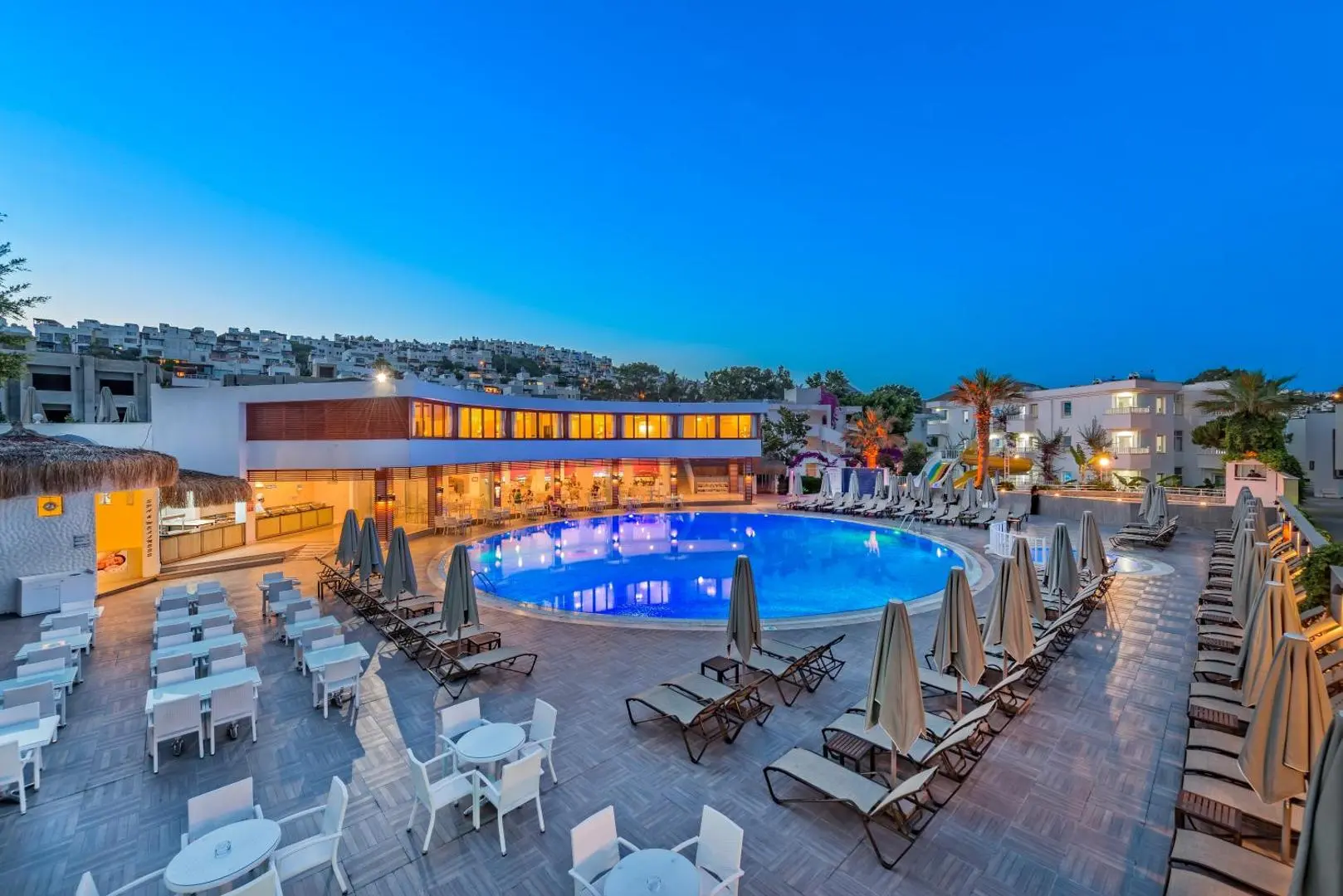 Басейн с шезлонги и чадъри, осветен във вечерния здрач – Bendis Beach Hotel, Бодрум