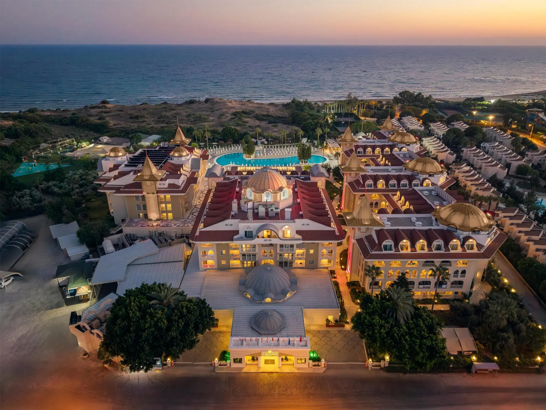 Хотелът с ярко осветена сграда и морето при залез от въздуха – Side Star Resort, Сиде