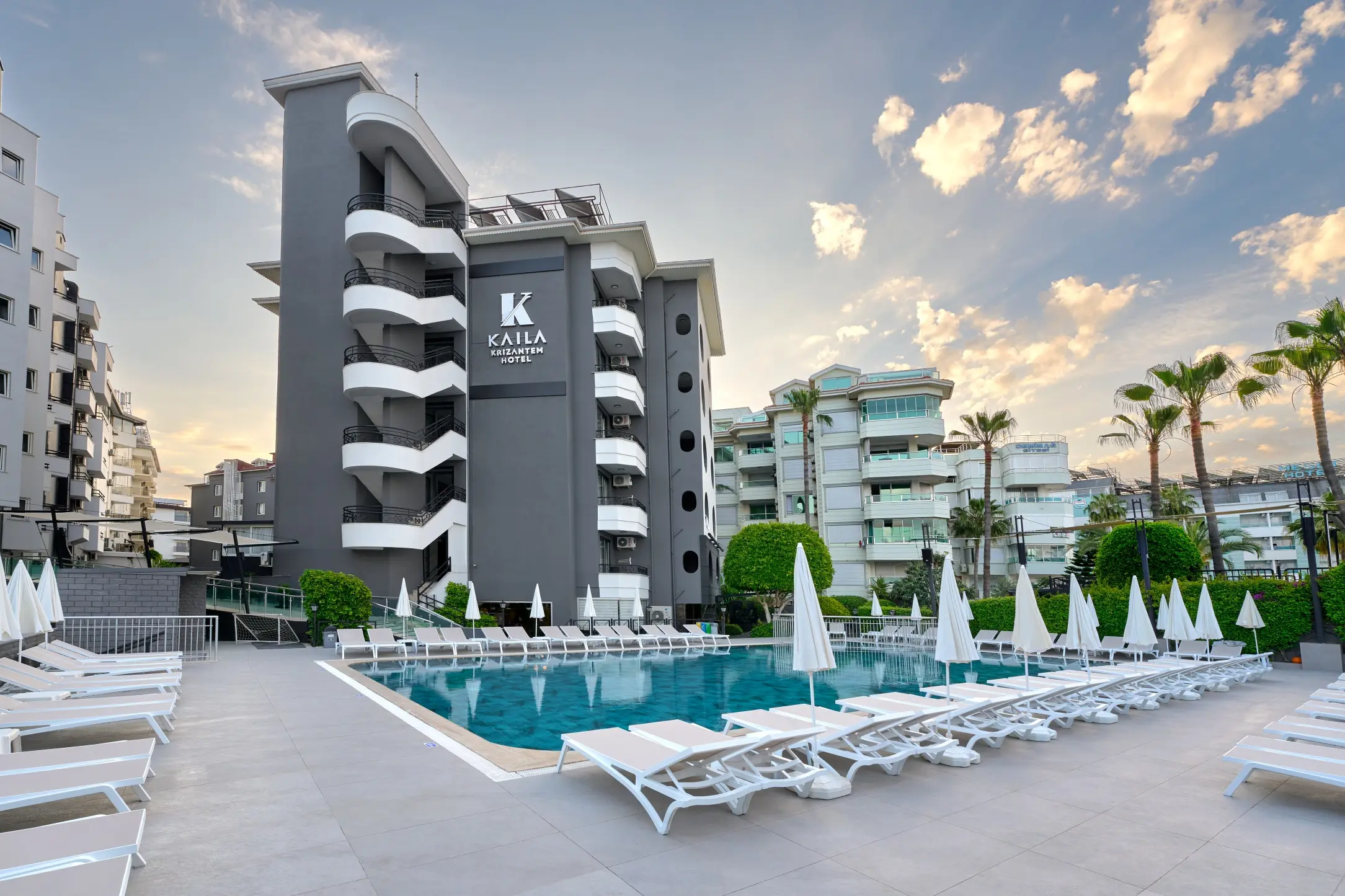 Тъмна сграда на хотела с логото на Kaila и басейн с бели шезлонги – Kaila Krizantem Hotel, Алания