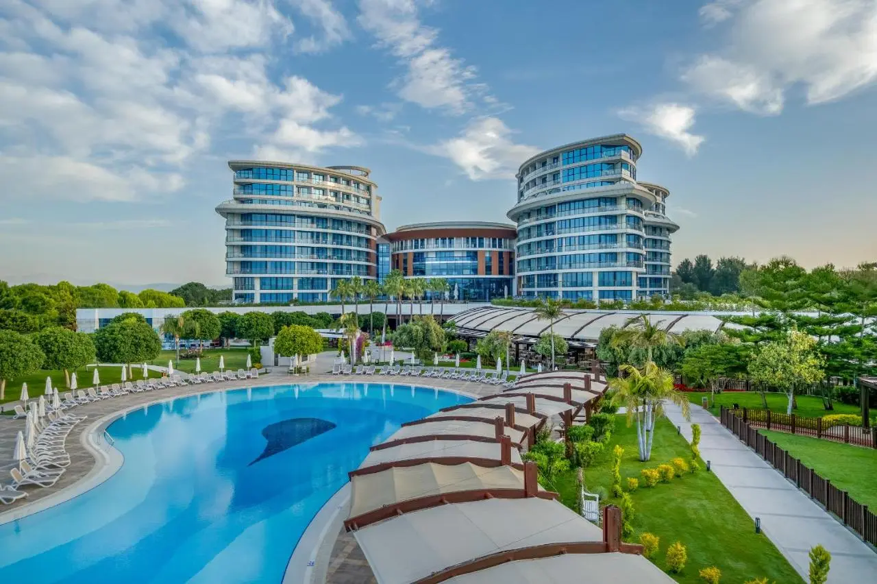 Басейн, градина и стъклените сгради на хотела под синьо небе – Baia Lara Hotel, Лара Кунду