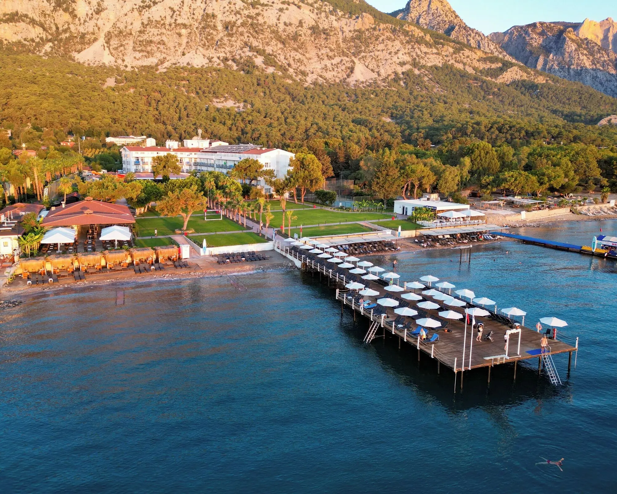 Въздушен изглед към дървен кей с чадъри и планина зад плажа – Transatlantik Beach Hotel, Кемер