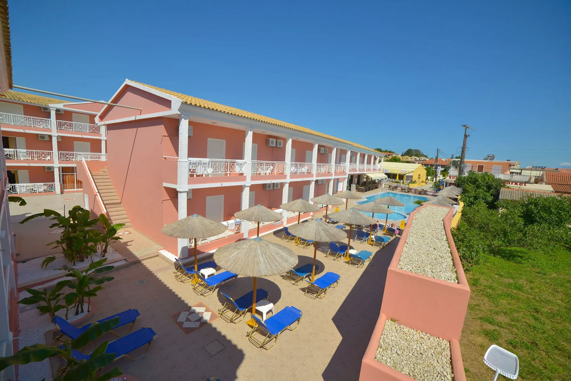 Розовите сгради и басейнът с чадъри отвисоко – Angelina Hotel & Apartments, Корфу