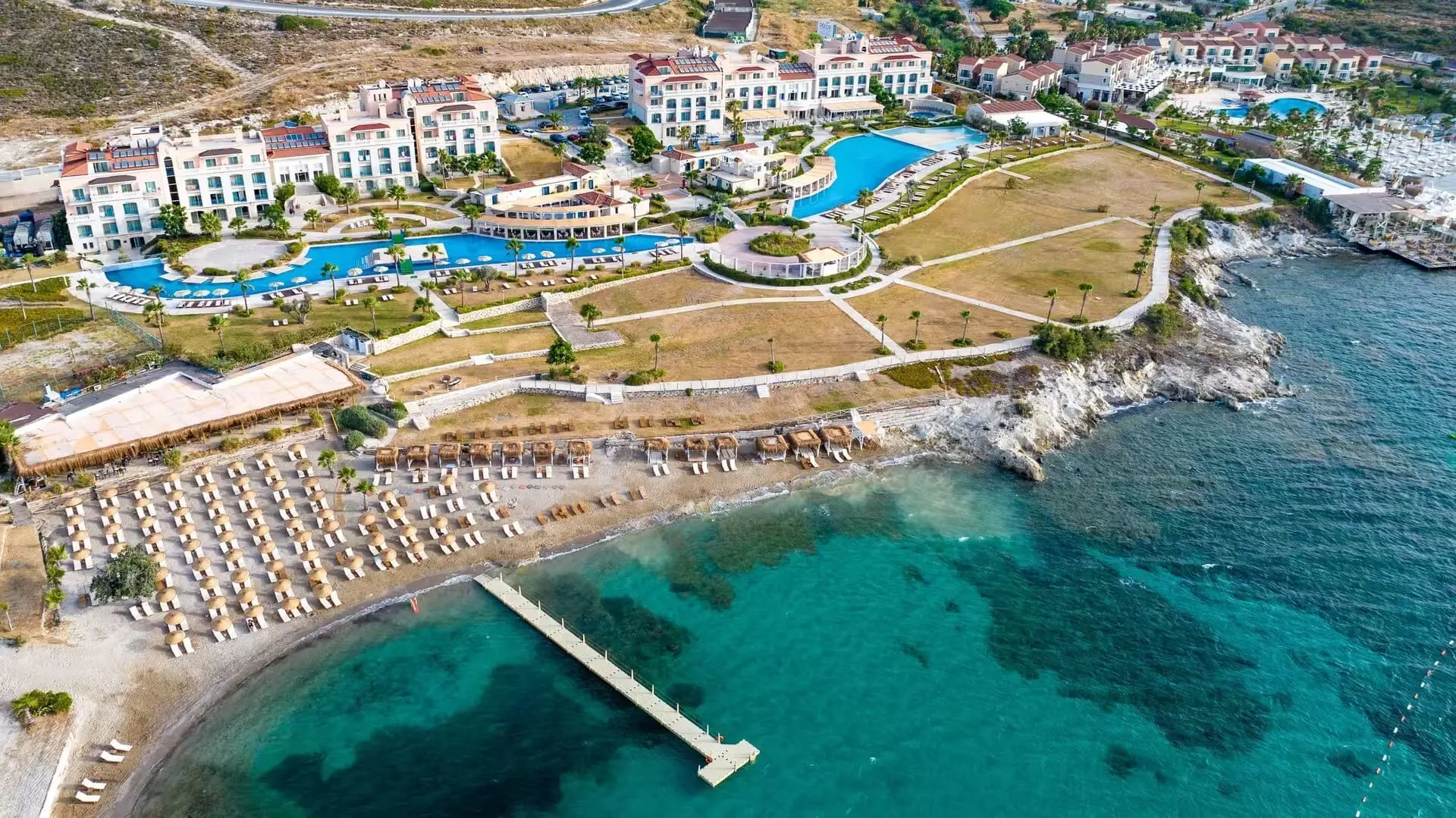 Въздушна гледка към залива с кей, плажа с чадъри и хотела – Dolce By Wyndham Cesme Alacati, Алачатъ
