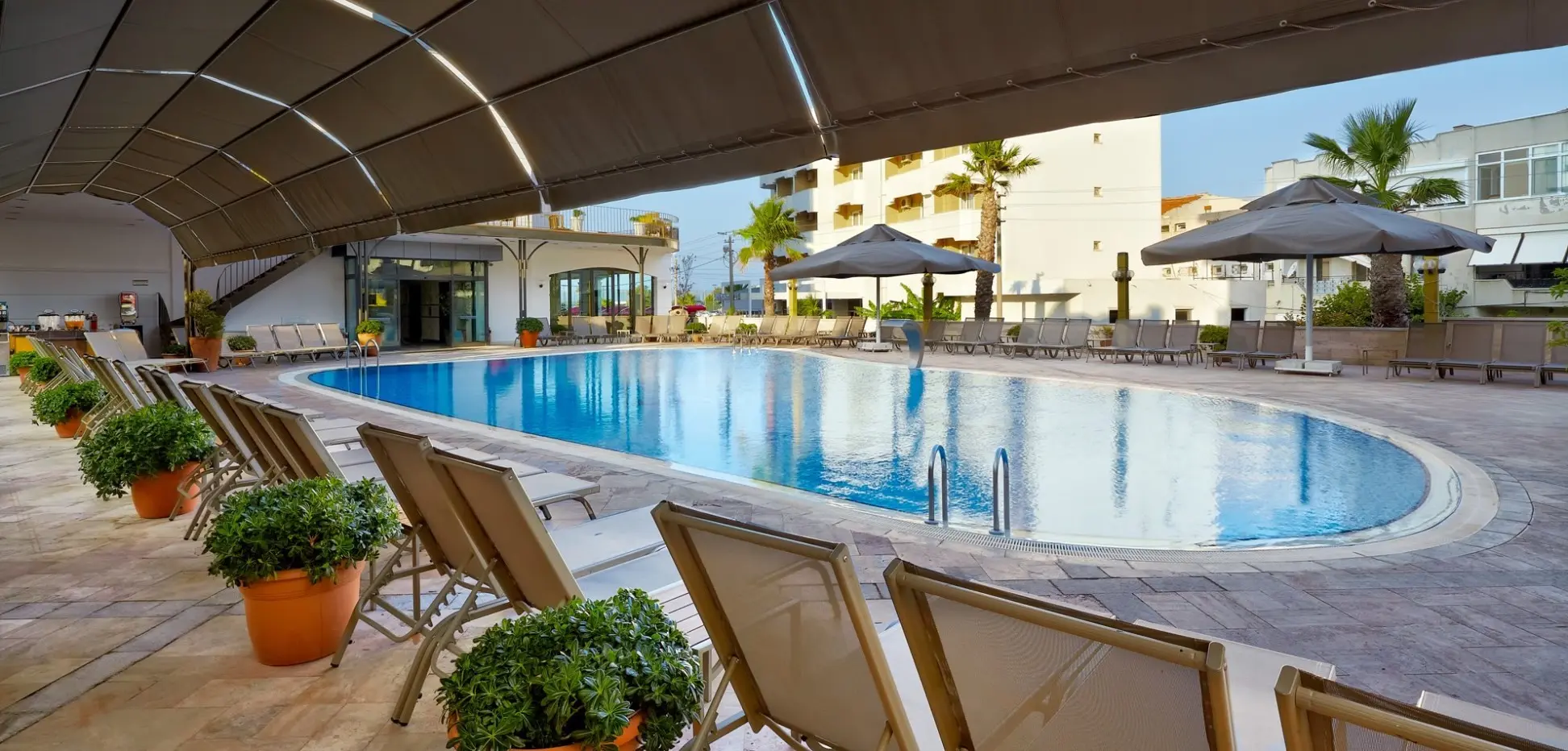 Изглед към басейна от покритата тераса с кресла и саксии – Cinar Hotel, Айвалък