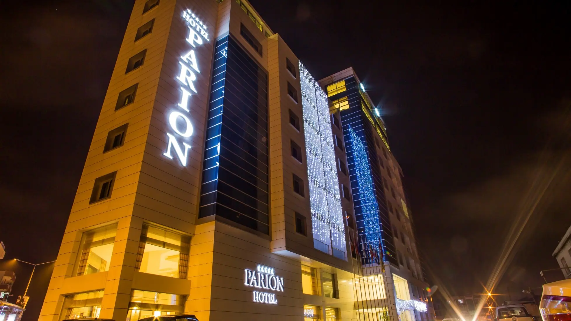 Фасада на хотела вечер с вертикален надпис Parion и синя подсветка – Parion Hotel, Чанаккале