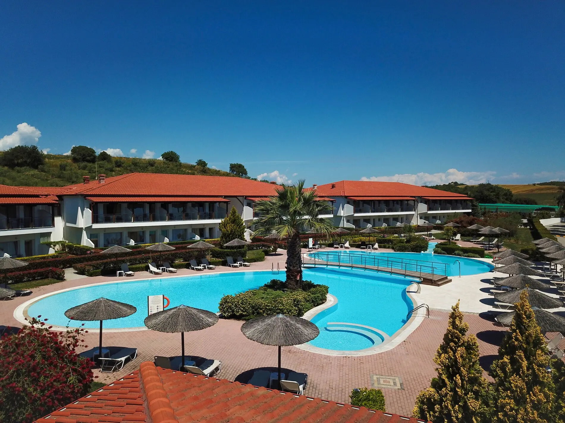 Басейнът с чадъри и сградите с червени покриви – Alexandros Palace Hotel & Suites, Атон