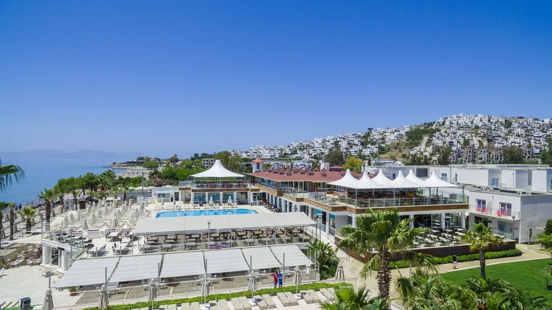 Басейн и бели шатри на брега, а зад тях белите къщи на Бодрум – Armonia Holiday Village & Spa, Бодрум