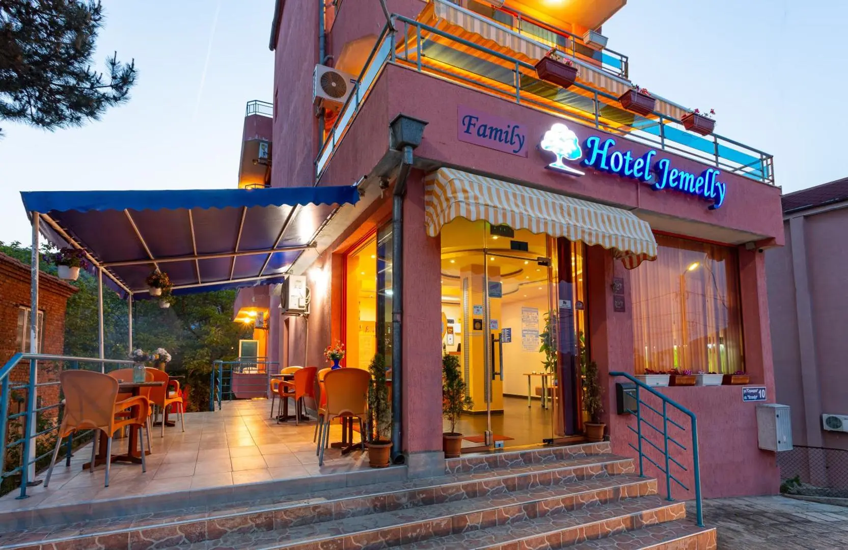 Вход с надпис Family Hotel Jemelly, стъпала и тераса с маси по здрач – Семеен хотел Джемелли, Обзор