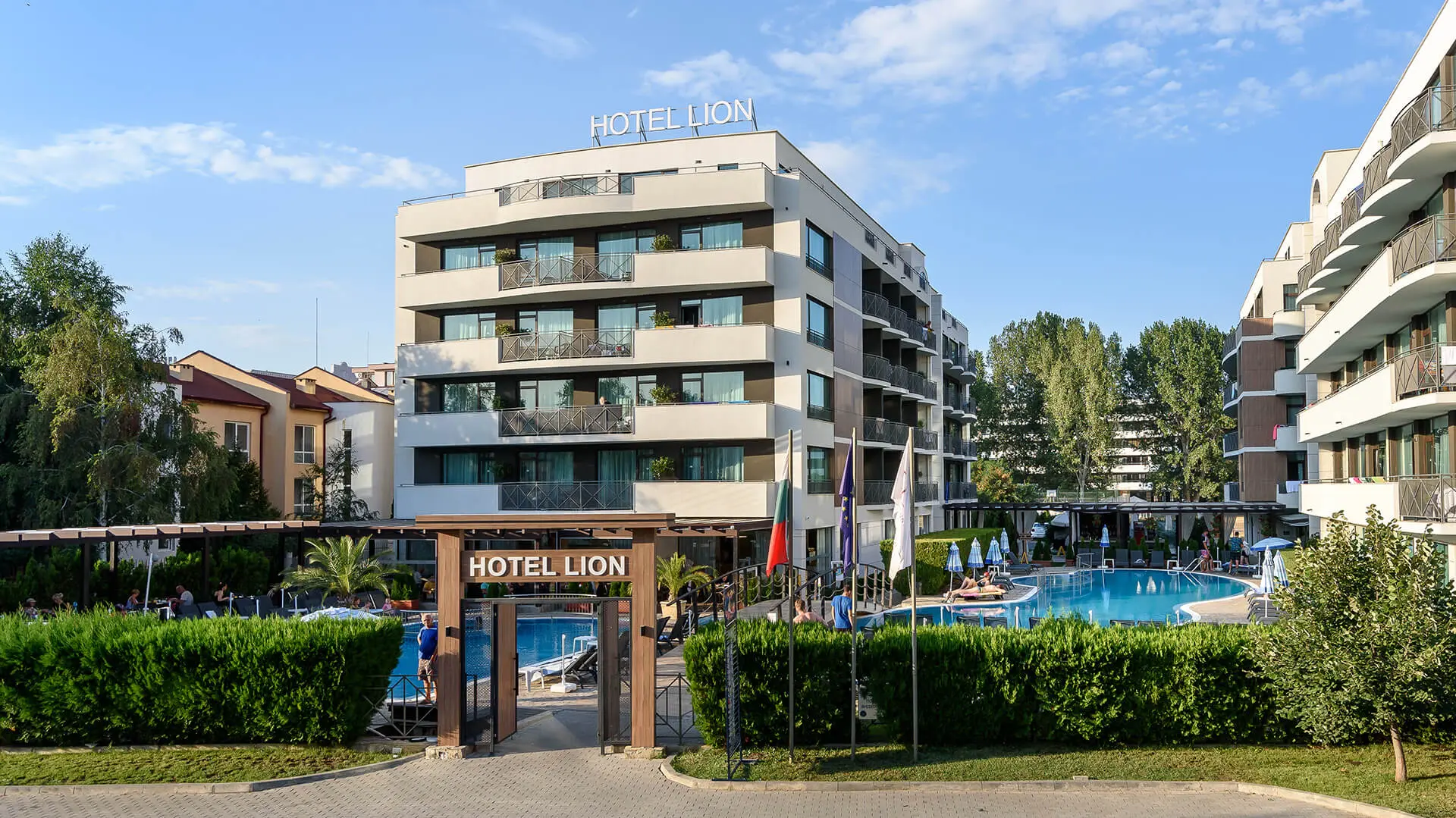 Входната арка с надпис Hotel Lion, басейнът и сградата на хотела в слънчев ден – Хотел Лион, Слънчев бряг