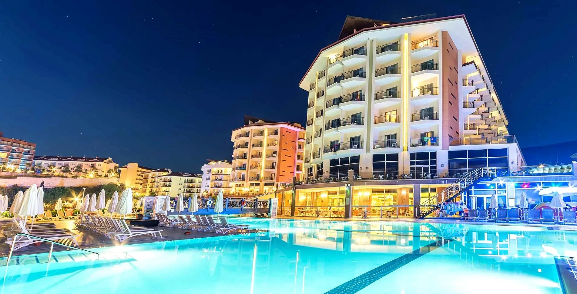 Хотелските сгради, осветени вечер, над открития басейн – Ramada Resort Kusadasi & Golf, Кушадасъ