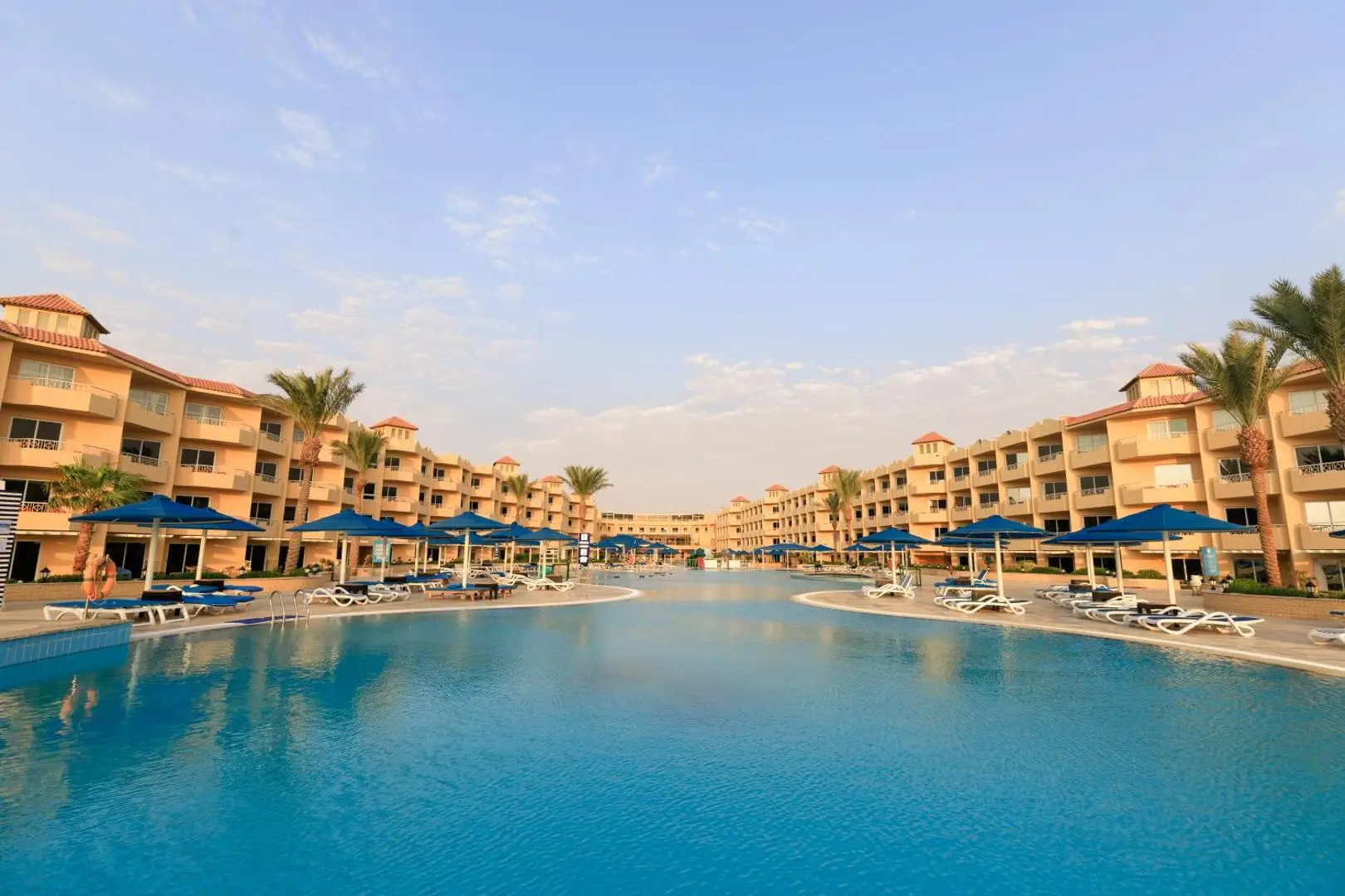 Голям басейн с шезлонги пред сградите на хотела по залез – Amwaj Beach Club, Хургада