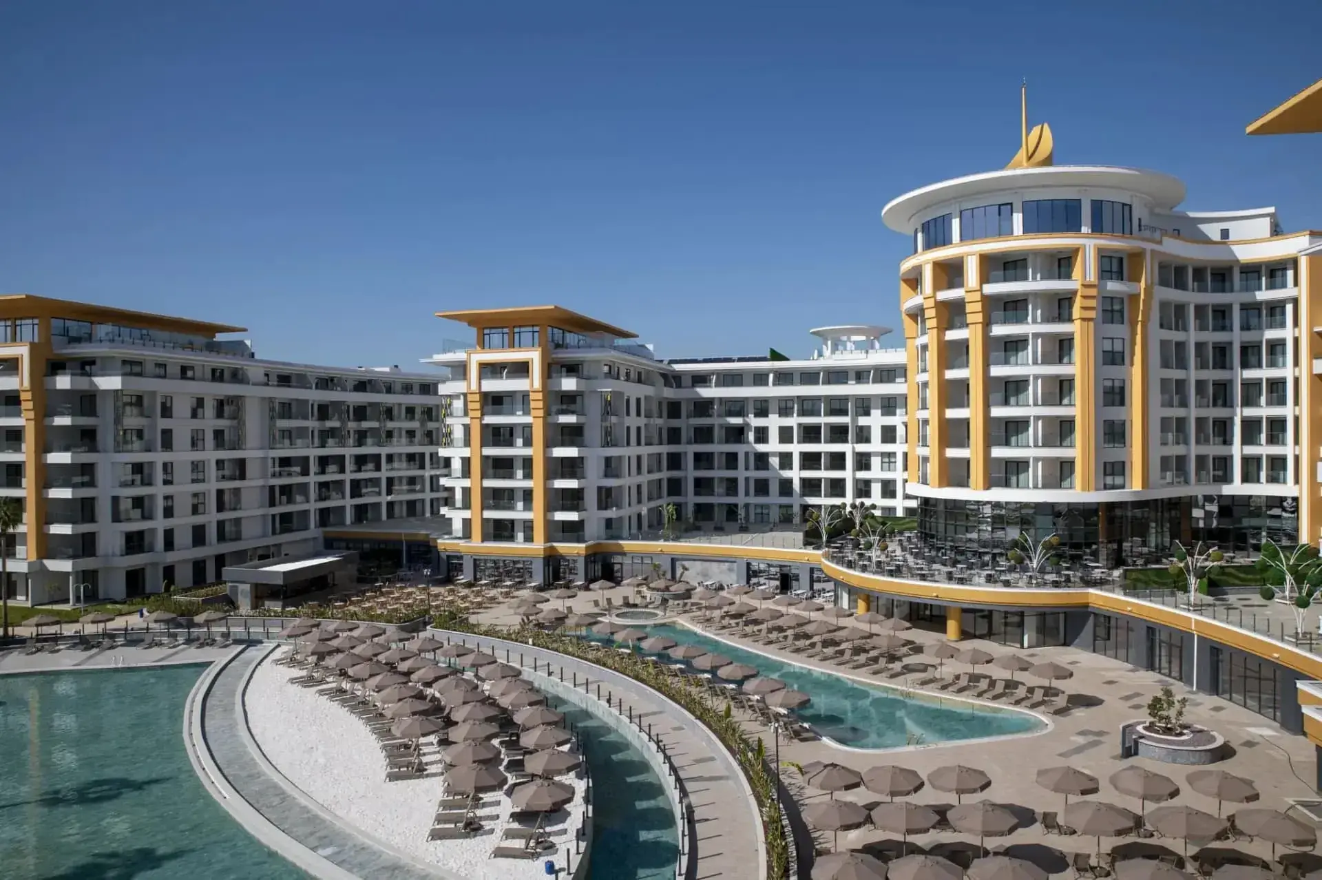 Хотелът с кулата и извитите басейни с шезлонги през деня – Azura World Hotel, Алания