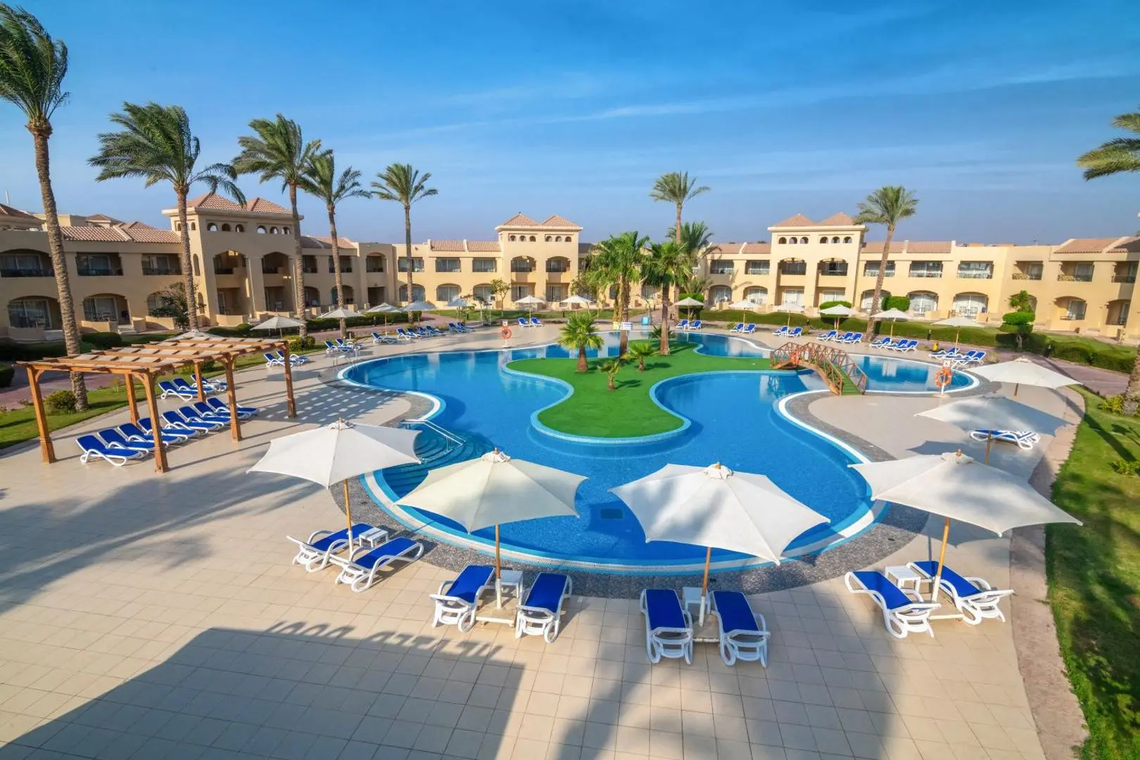 Голям басейн с островче, бели чадъри и шезлонги сред палми – Cleopatra Luxury Resort Makadi Bay, Макади Бей