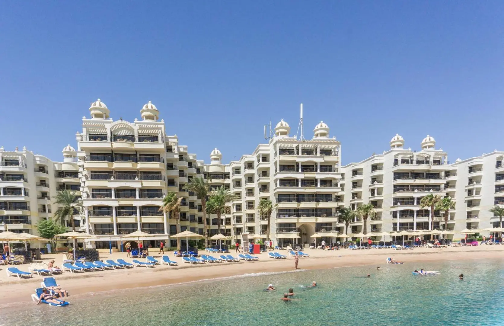 Белите сгради на хотела над пясъчния плаж в лагуната с плуващи гости – Sunrise Holidays Resort (16+), Хургада
