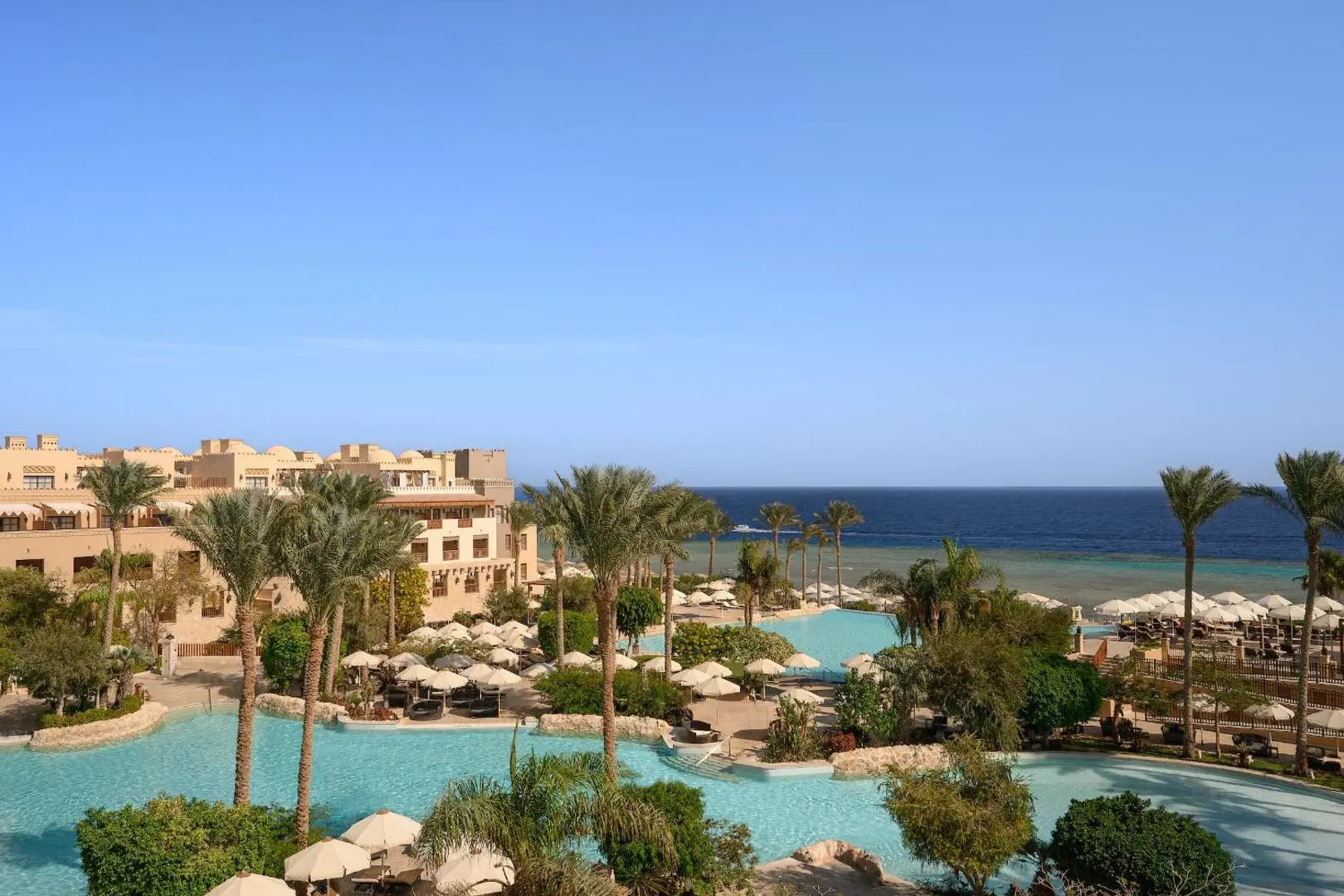 Панорама на басейна с палми и морето зад сградите – The Makadi Spa Hotel, Макади Бей