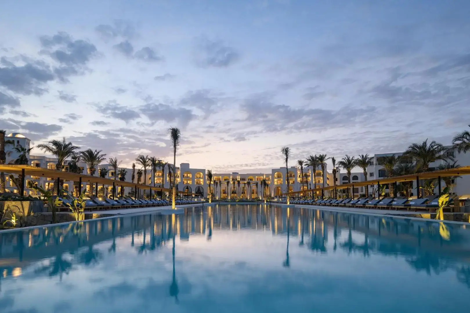 Голям басейн при залез, обграден от палми и шезлонги – Serry Beach Resort, Хургада