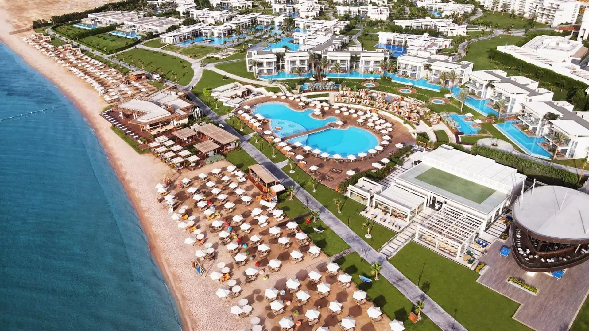Панорама отгоре на плажа с чадъри, басейните и спортните терени – Rixos Premium Magawish Suites & Villas, Хургада
