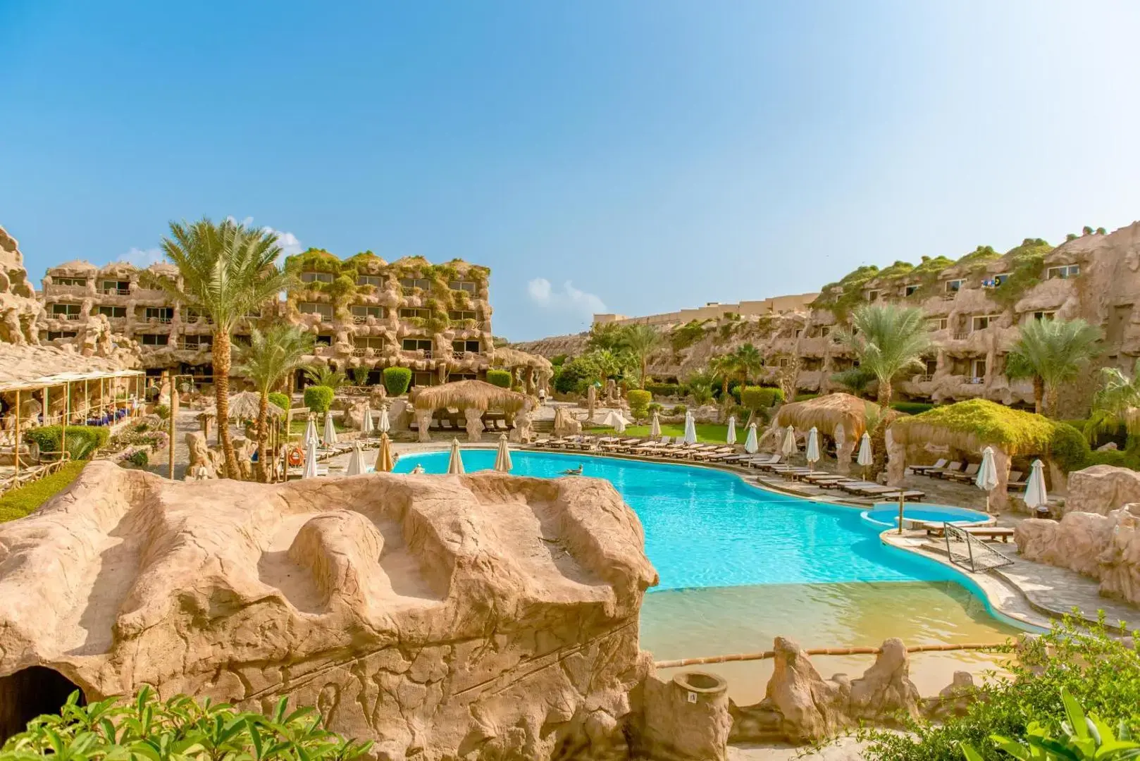 Басейн сред скални форми и палми пред сградите в пещерен стил – Caves Beach Resort Hurghada (Adults Only 16+), Хургада