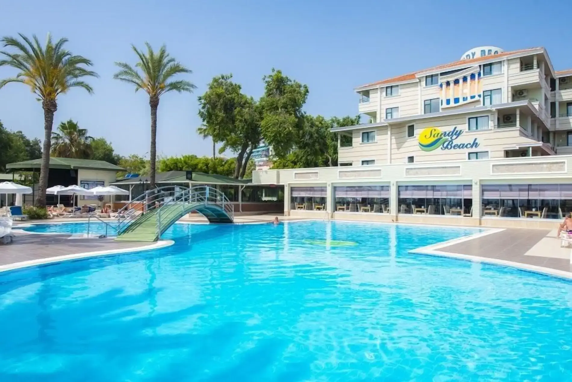 Хотелът и басейнът с палми и зелено мостче отляво – Sandy Beach Hotel, Сиде