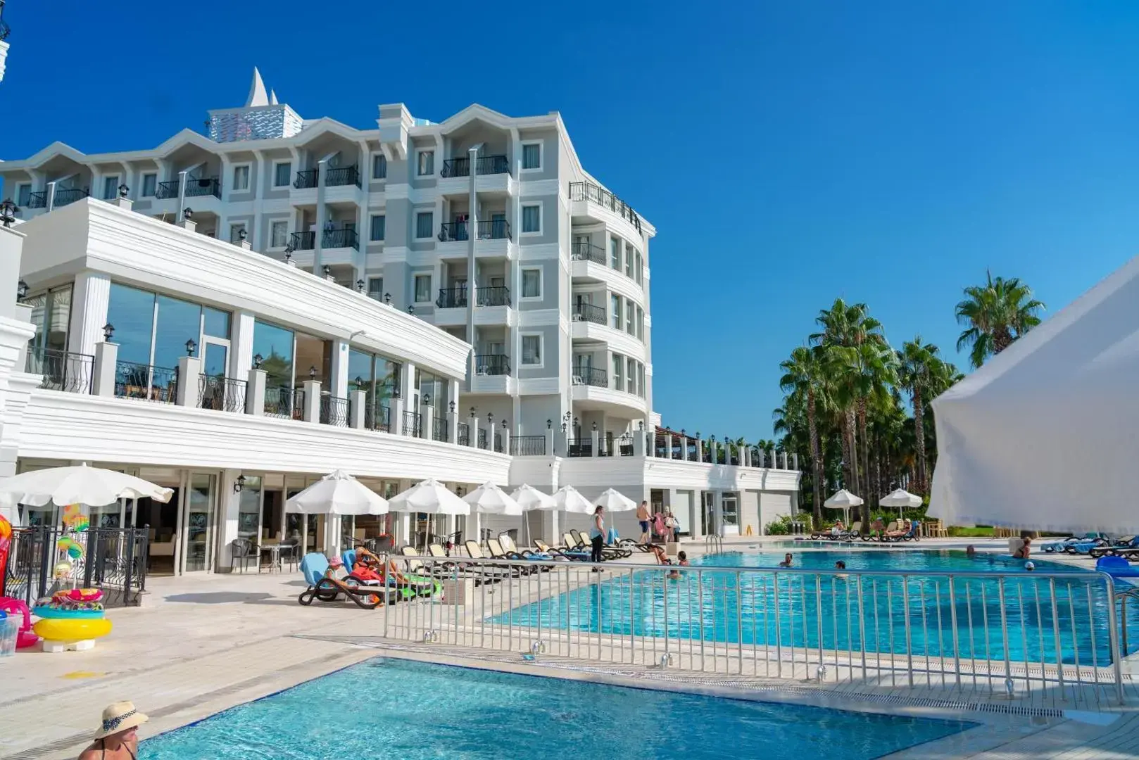 Хотелската сграда и басейнът с ограда под синьо небе – Royal Atlantis Beach, Сиде