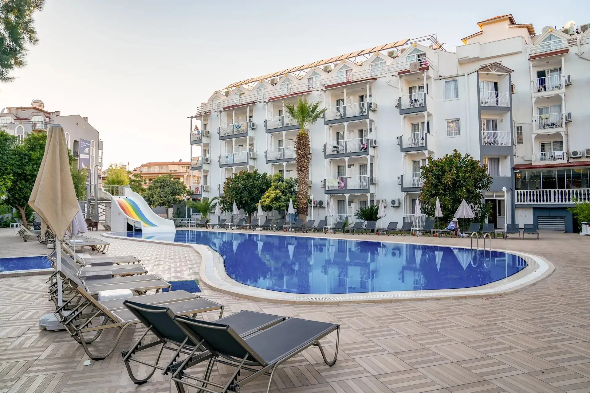 Овален басейн с шезлонги пред бялата сграда с балкони – Halici Hotel, Мармарис
