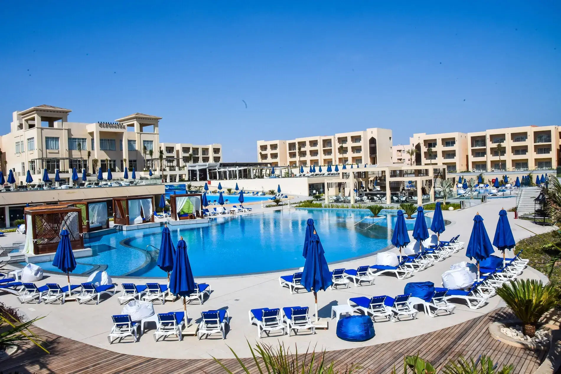 Голям басейн със сини чадъри и шезлонги пред сградите – Cleopatra Luxury Resort Sharm Adults Only (16+), Шарм Ел Шейх