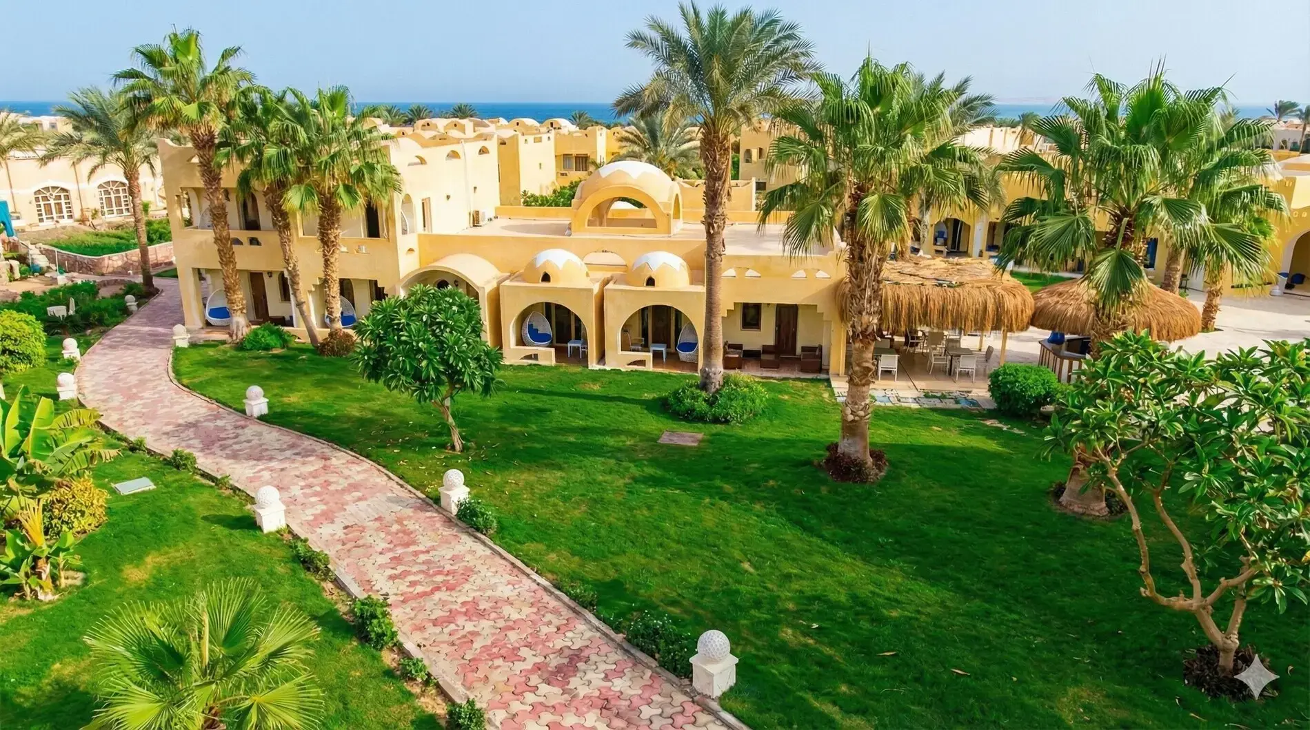 Алея през зелена морава с палми пред двуетажните сгради и морето – Romance Regency Club (16+), Шарм Ел Шейх