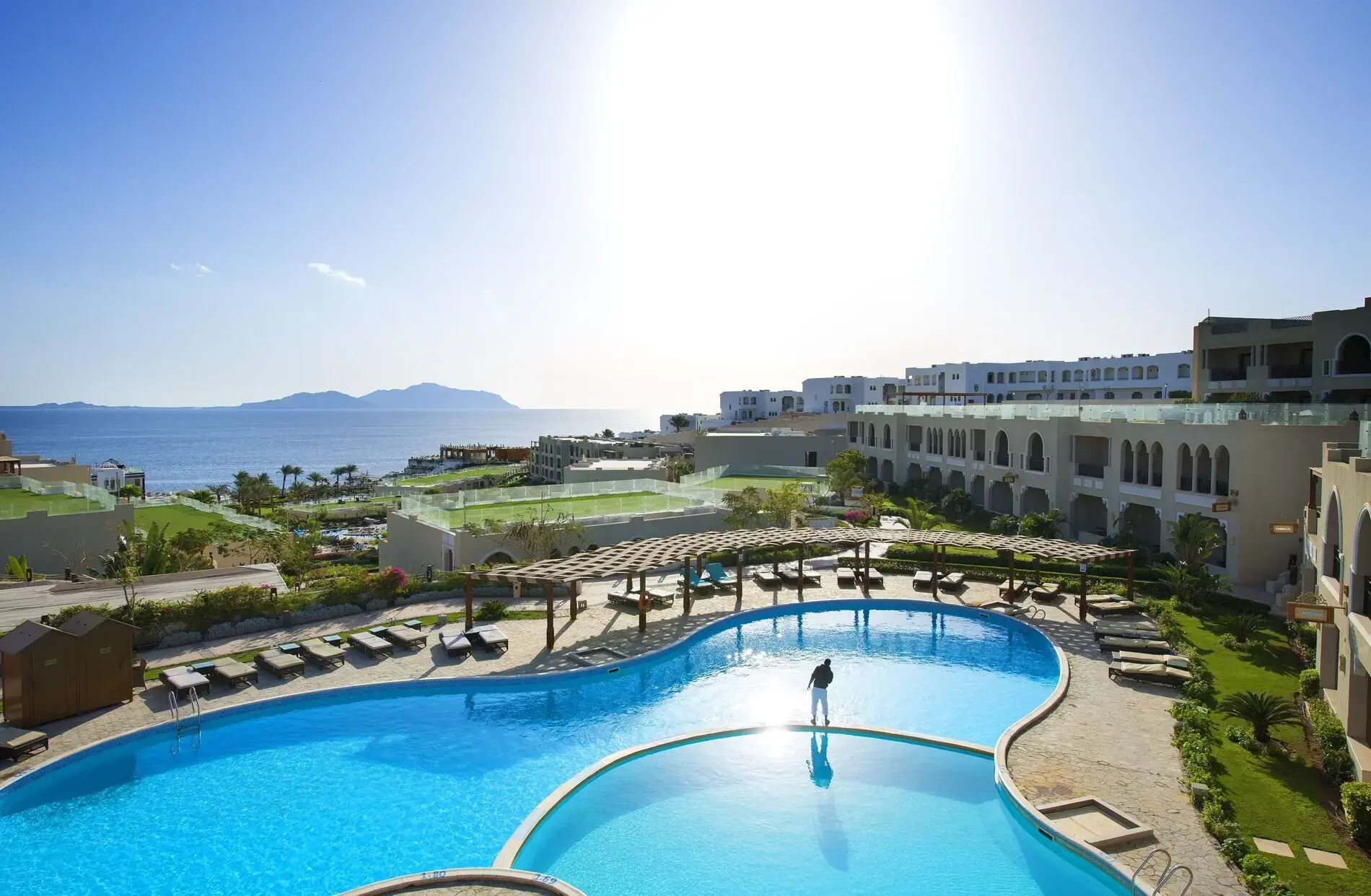 Извит басейн, сгради на брега и планини отсреща – Posh Club - Sunrise Arabian Beach Resort, Шарм Ел Шейх
