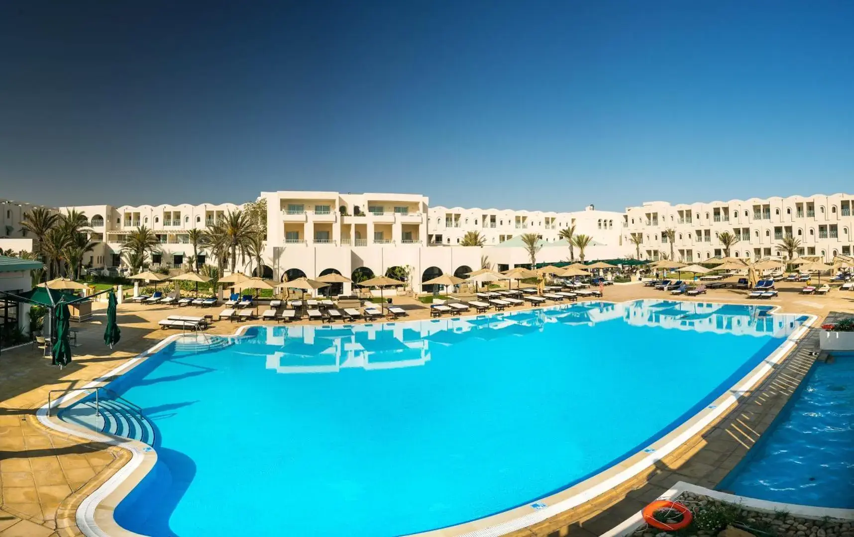 Голям открит басейн с шезлонги пред белите сгради на хотела – Ulysse Djerba Thalasso & Spa, Джерба