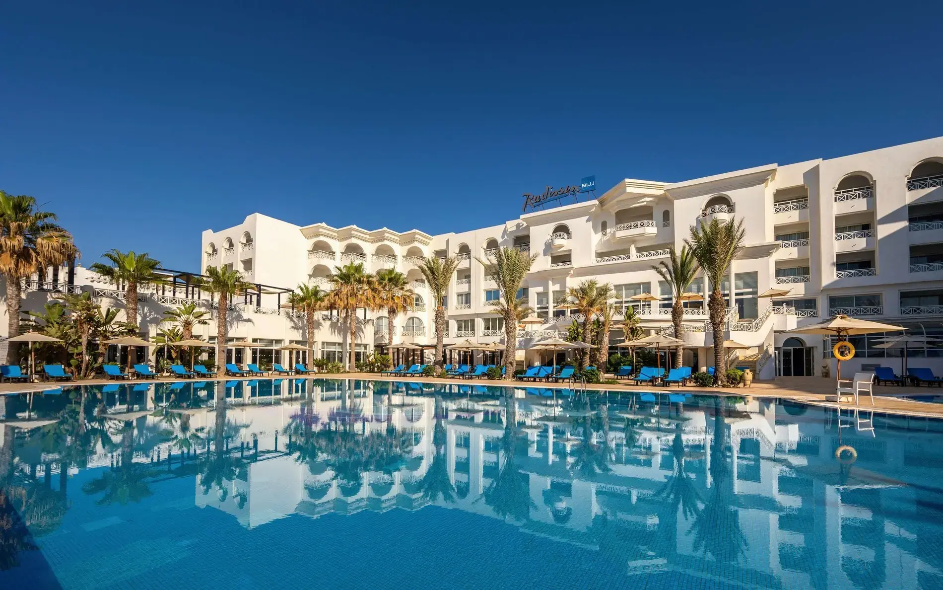 Бялата сграда на хотела над открития басейн – Radisson Blu Resort & Thalasso Hammamet, Хамамет