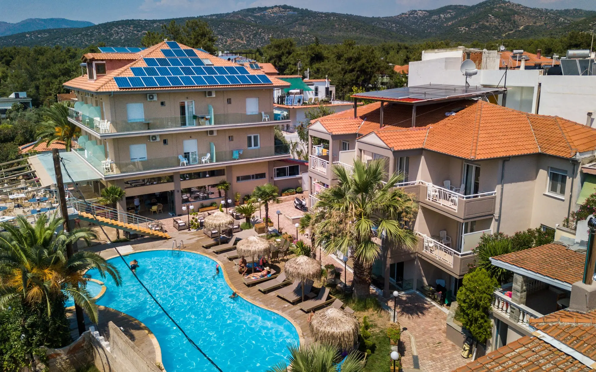 Басейнът и сградите на хотела сред палми и планини – Hotel Potos, Тасос